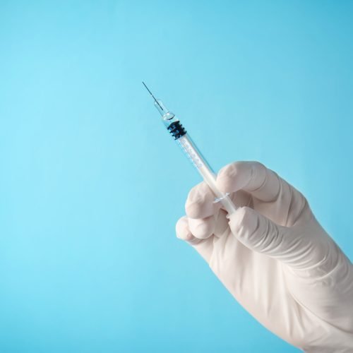 Hand of nurse with syringe prepared for vaccination, on color background
