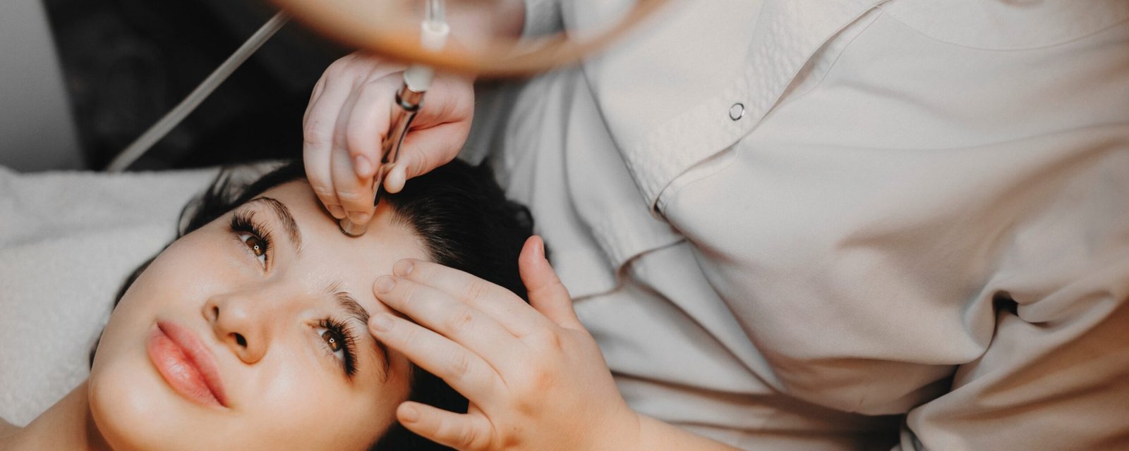 Upper view lovely female face leaning on a spa bed with eyes opened doing noninvasive microdermabrasion on her face by a cosmetologist in a spa center. girl having microneedling done on forhead