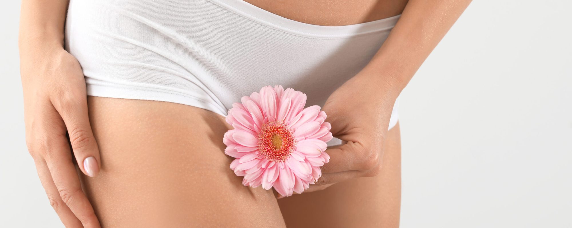 Young woman with flower on grey background, closeup. Gynecology girl covering private spot with flower/ vaginal prp photo